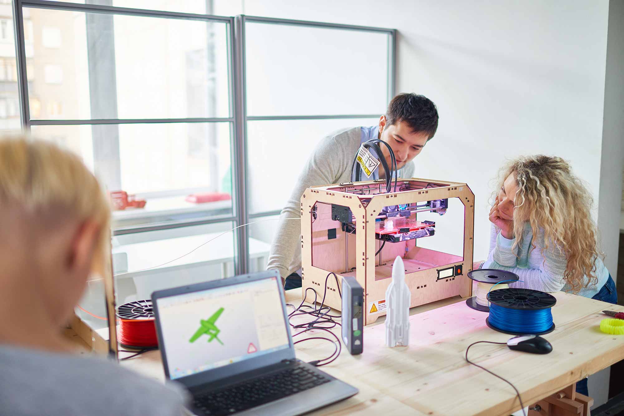 Group of young engineers making prototype of plane with 3D printing in technology laboratory and observing process