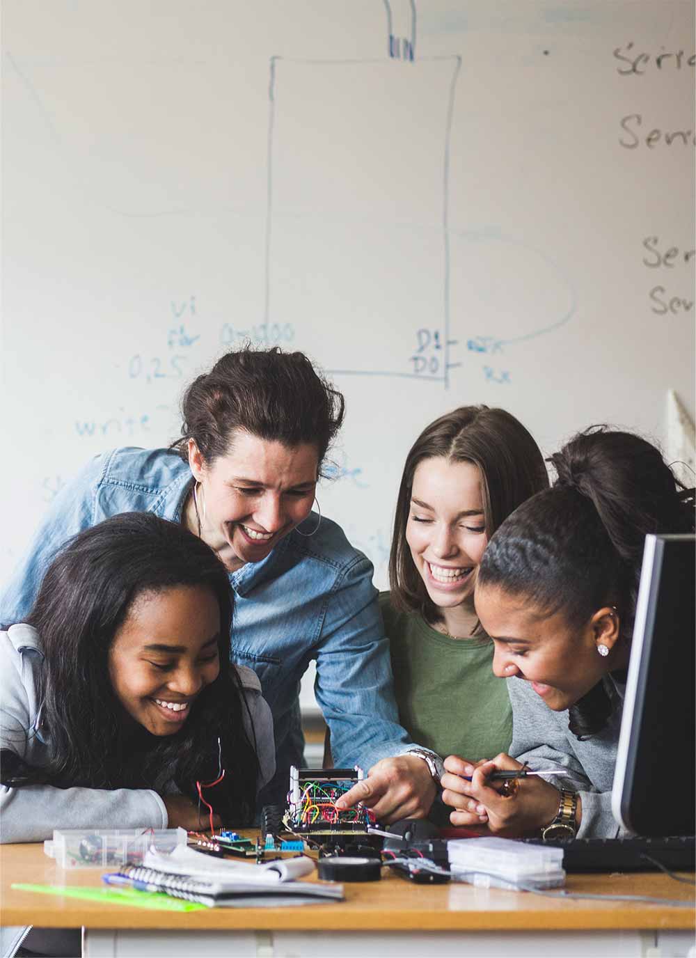 Smiling female teacher and high school teenage students preparing robot on desk in classroom