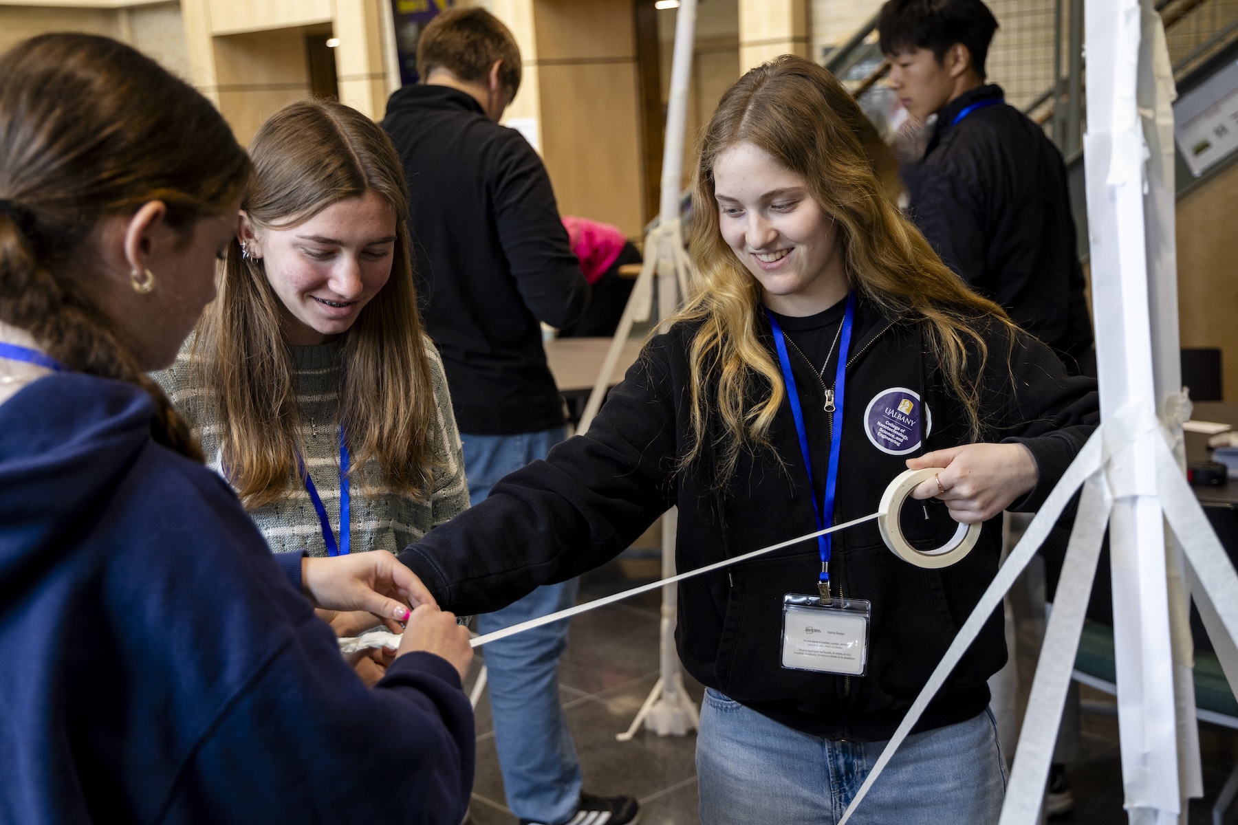 Riley Dewolf, Adelle Coburn and Harper Frisbee look down at outstretched masking tape.