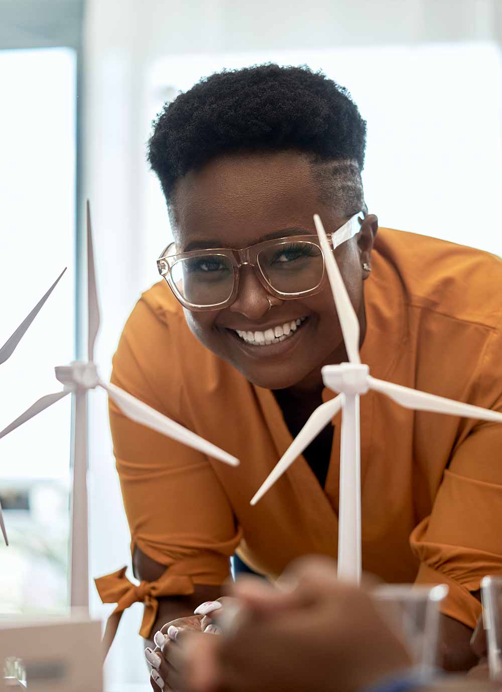 Smiling woman leaning on desk in front of model windmills 