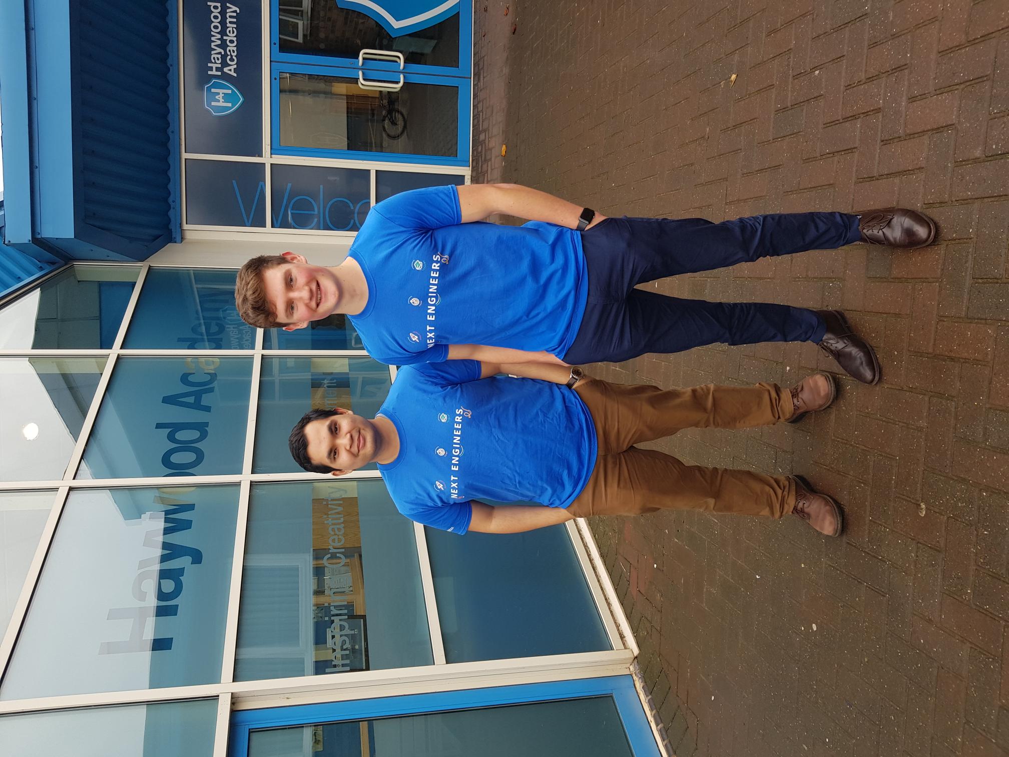 Two General Electric volunteers are wearing blue GE t-shirts and standing outside a school.