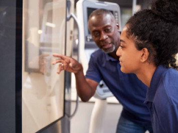 Engineer Showing Apprentice How To Use CNC Tool Making Machine